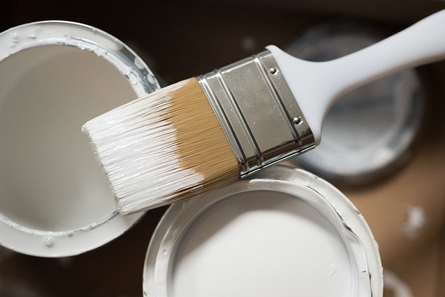 A paint bucket and a paintbrush dipped in white paint.